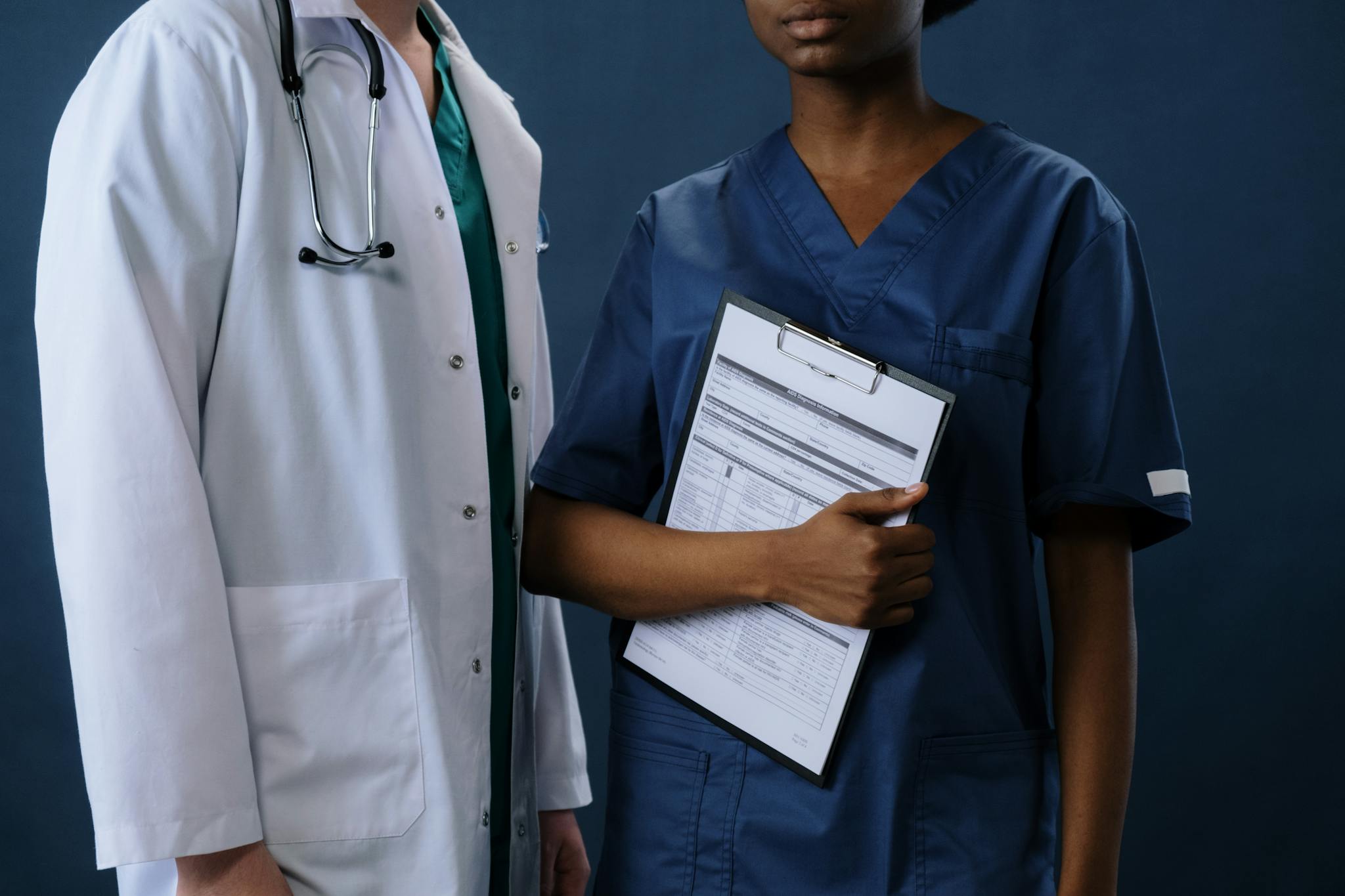 Two healthcare professionals in scrubs and lab coat with a clipboard, representing teamwork.