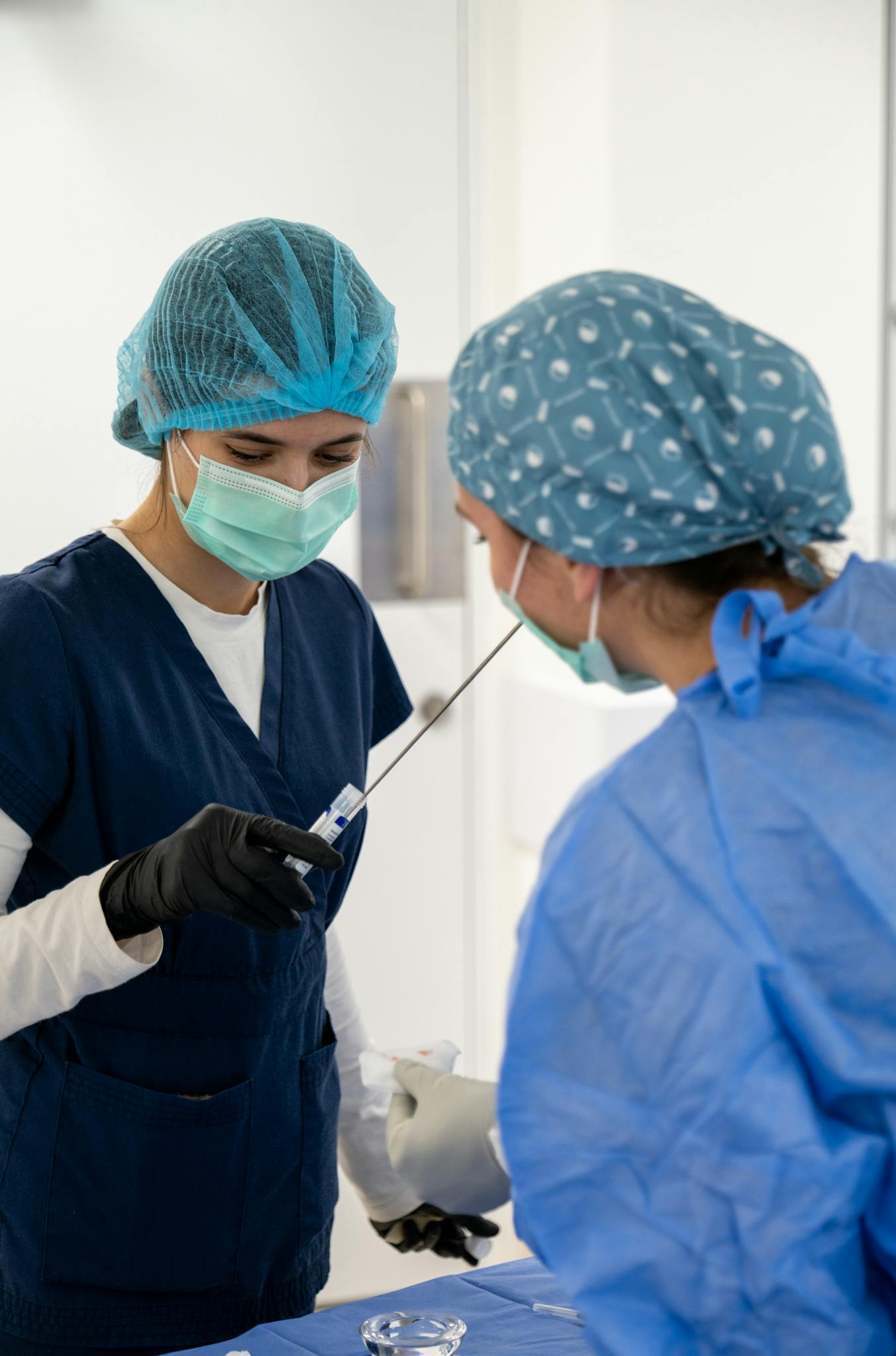 Two nurses in full PPE performing a medical procedure in a hospital setting.